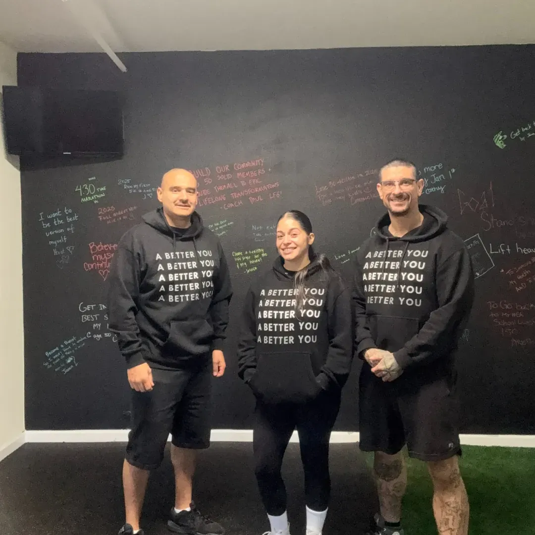 The coaching team in A Better You hoodies in front of the gym's chalk wall